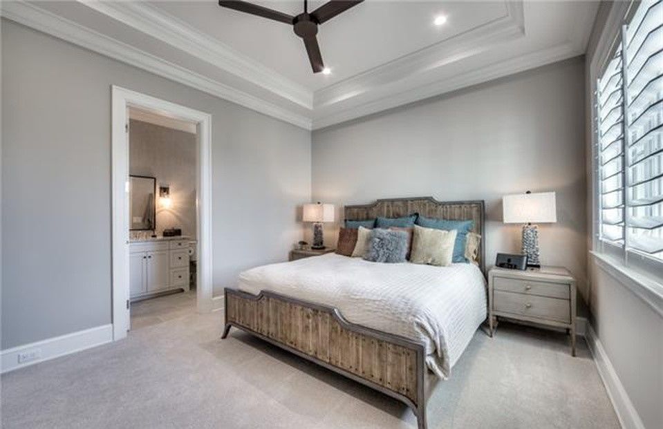 Bedroom with a wooden bed, nightstands, and window with shutters. Light gray walls, ceiling fan.