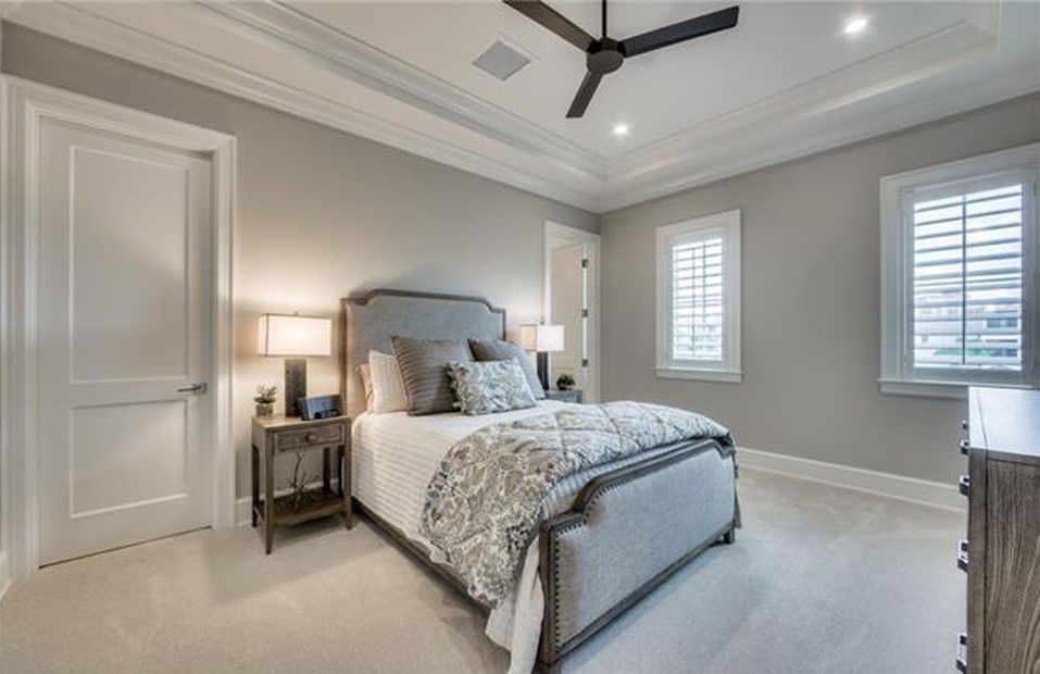 Bedroom with a gray bed, white door, and shutters. Light gray walls and ceiling fan.