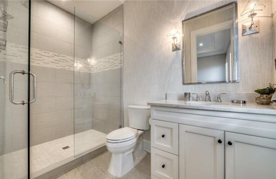 Bathroom with glass shower, white vanity, and toilet; gray and white tile, modern design.
