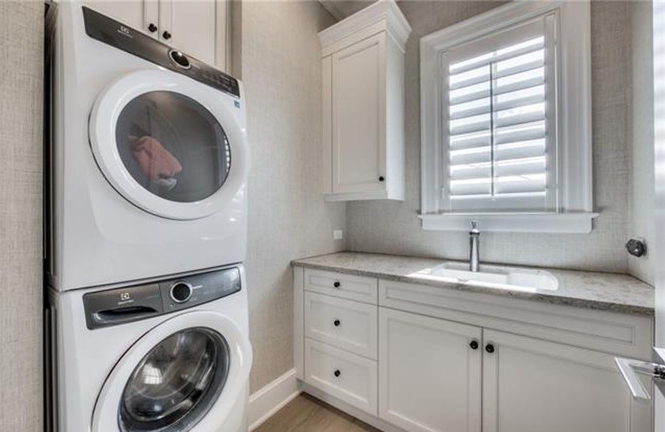 White laundry room with stacked washer/dryer, white cabinets, and a sink.
