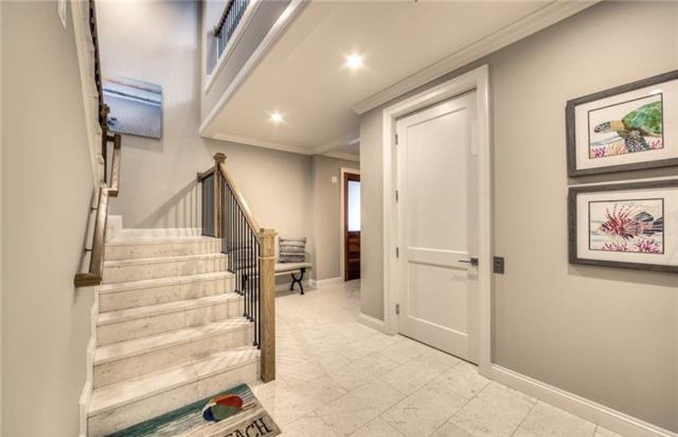 Hallway with staircase, white door, and artwork on the wall. Light gray walls and flooring.
