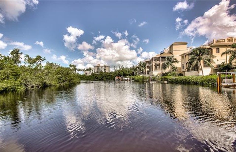 Waterway with buildings, docks, and trees under a cloudy blue sky.