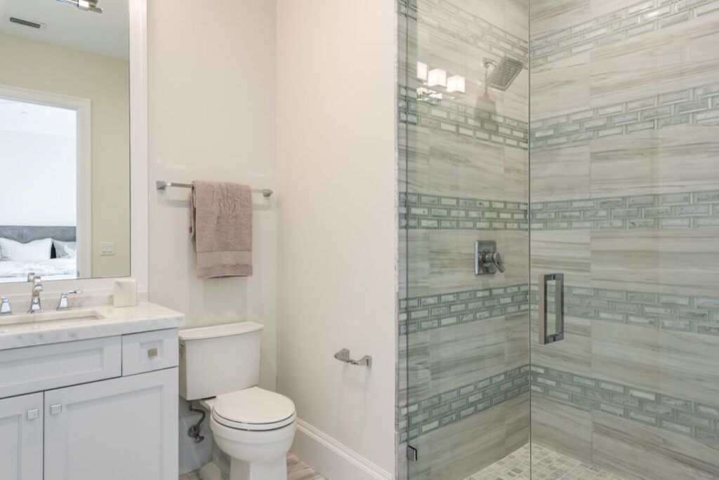 Bathroom with a white vanity, toilet, and glass shower. Gray tile and pale blue accents.