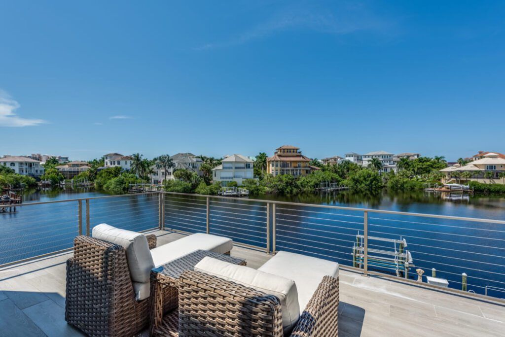Patio with wicker furniture overlooking a canal lined with waterfront homes under a clear blue sky.