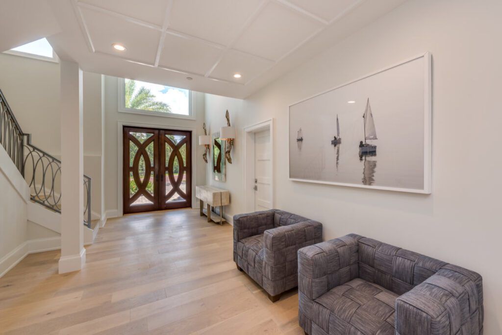 Spacious entry hall with wood floors, two gray armchairs, large sailboat art, and double door entrance.