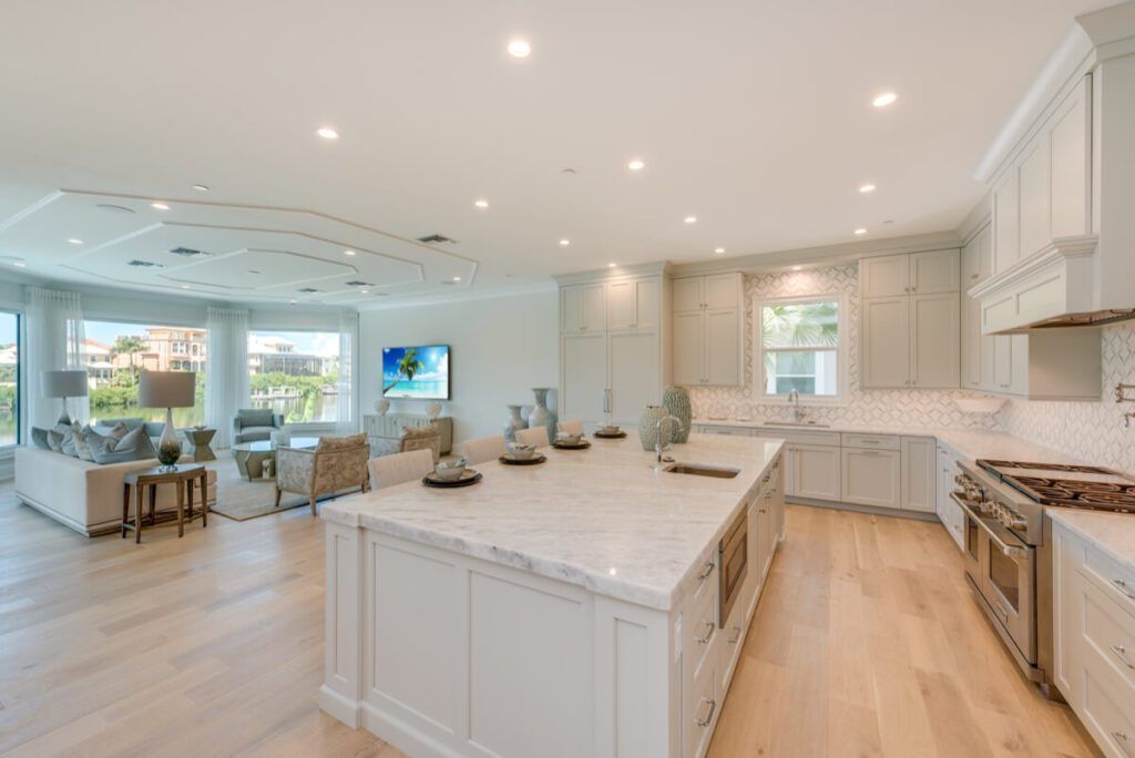 Open-concept kitchen and living area with light wood floors, white cabinets, and a marble island.