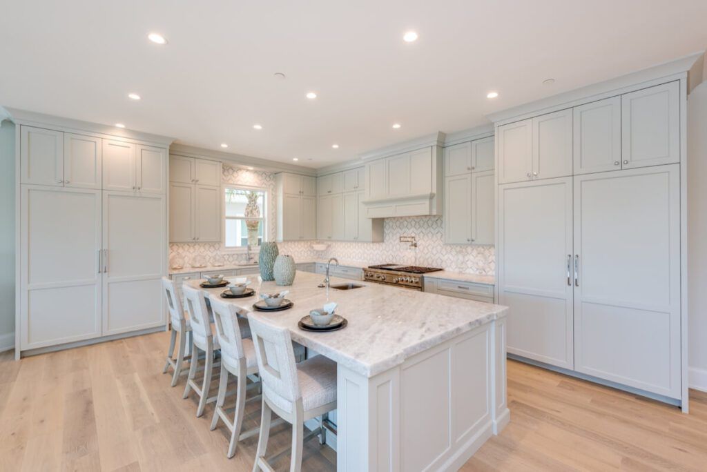Bright, modern kitchen with pale blue cabinets, marble countertops, and a central island with seating.