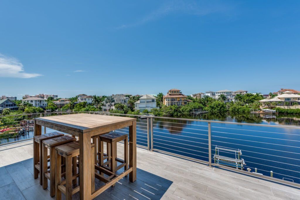 Rooftop deck with a wooden table and stools, overlooking water and houses on a sunny day.