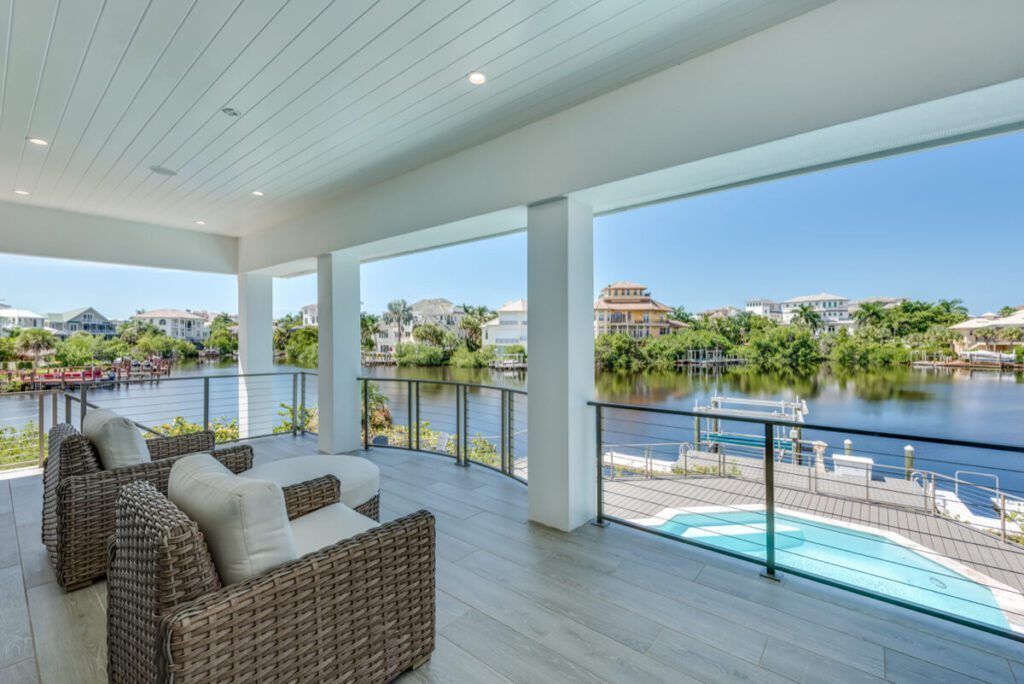 Covered patio overlooking water, featuring wicker chairs and a small pool.
