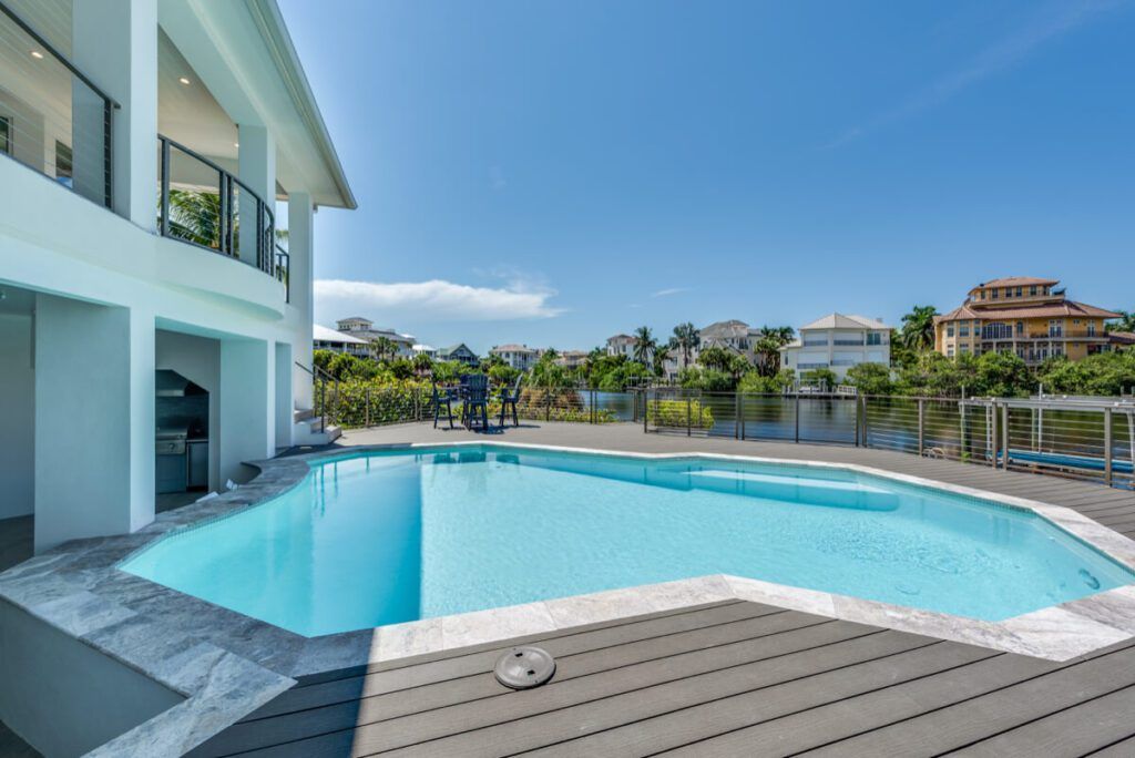 A modern house with a blue swimming pool and a sunny view of a canal and other houses.