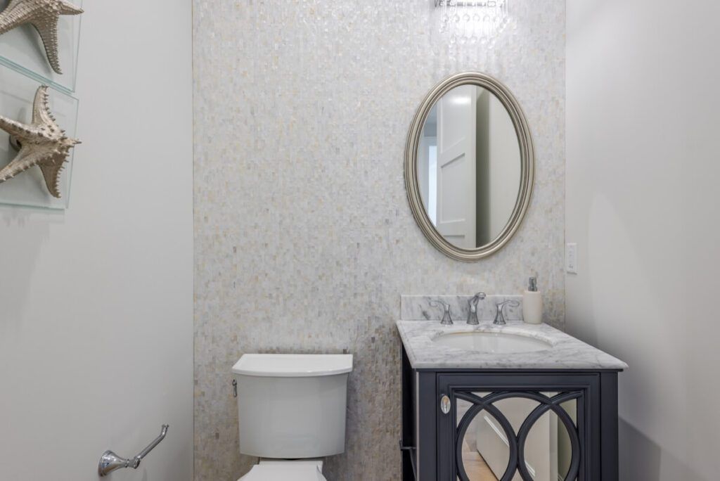 Bathroom with toilet, vanity, oval mirror, and patterned tile accent wall.