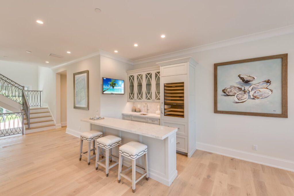A bar area with a countertop and stools, TV, cabinets, and a stairwell with wooden flooring.