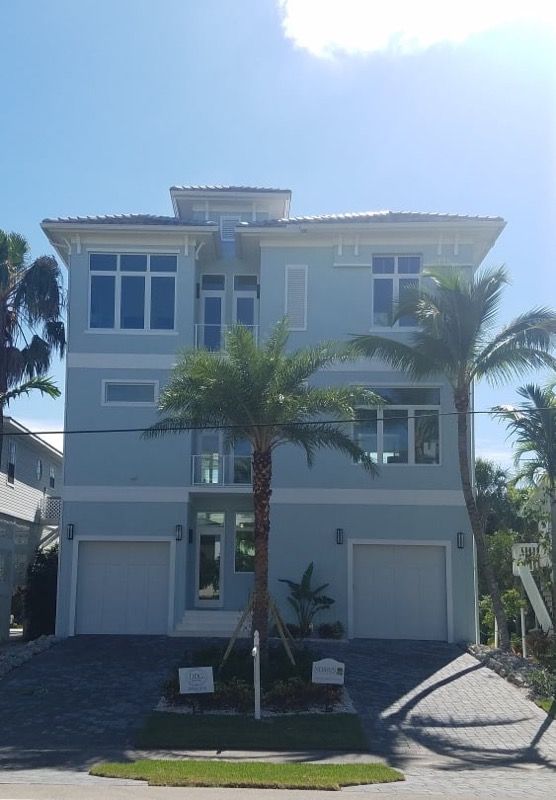 Light blue multi-story house with palm trees, two-car garage, and a light blue sky.