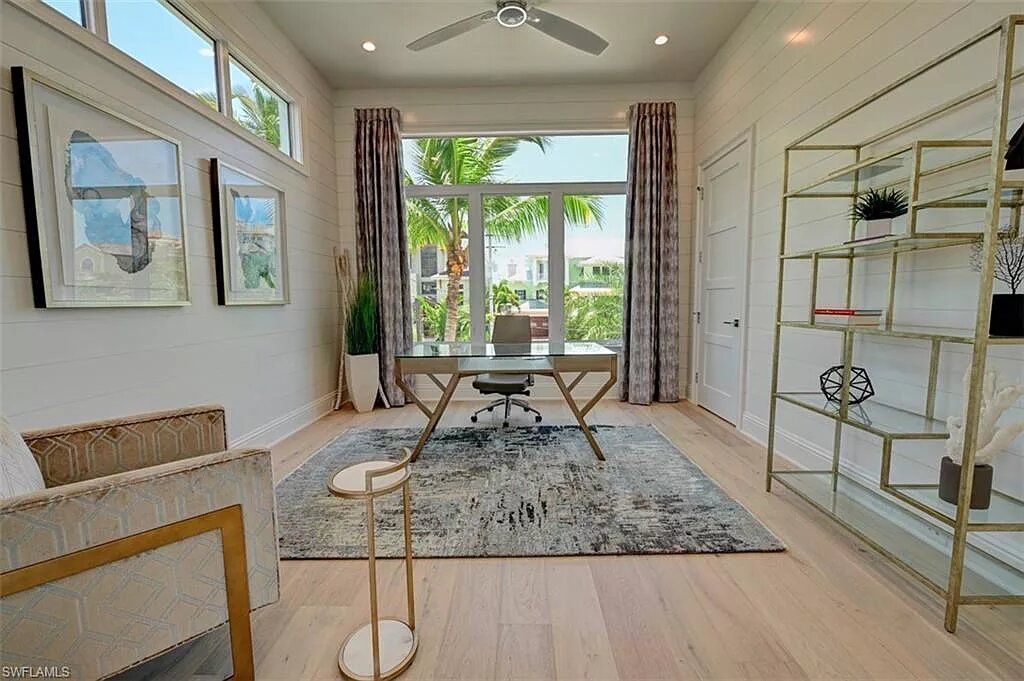 Home office with large window, desk, bookcase, chairs, and patterned rug.