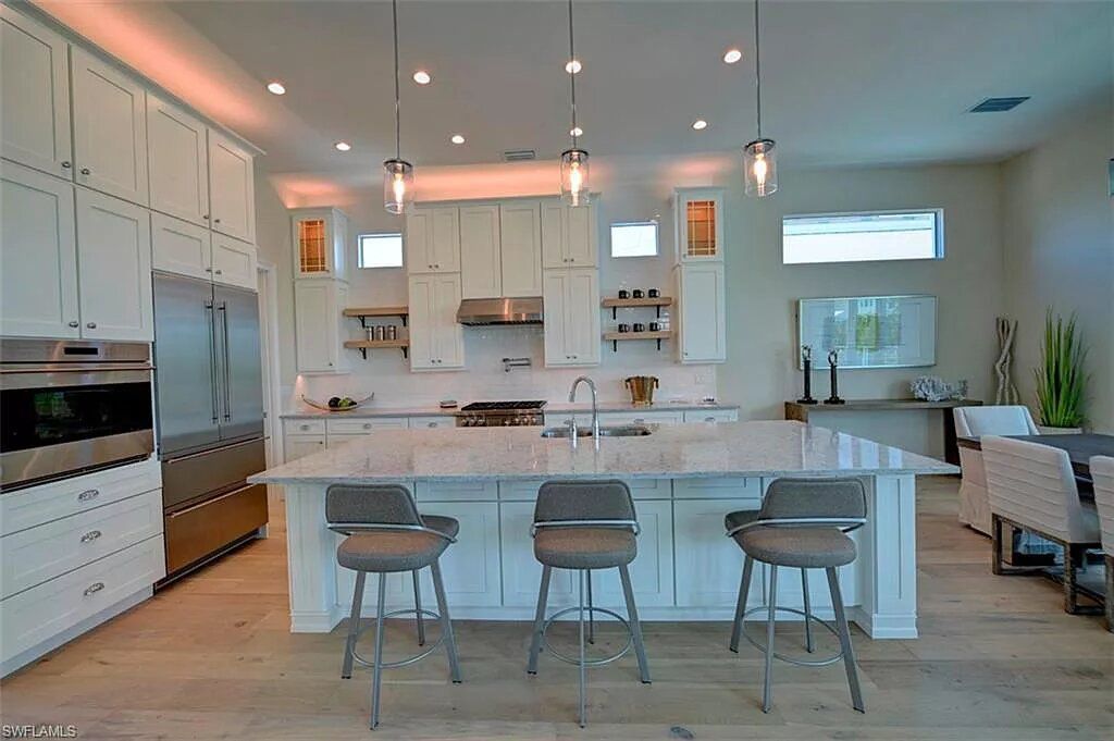 Modern kitchen with white cabinets, marble island, stainless steel appliances, and pendant lights.