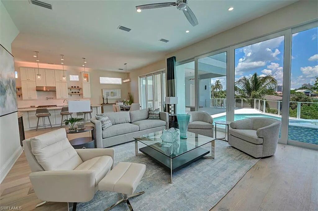 Living room with pool view, white furniture, large windows, and open-plan kitchen.