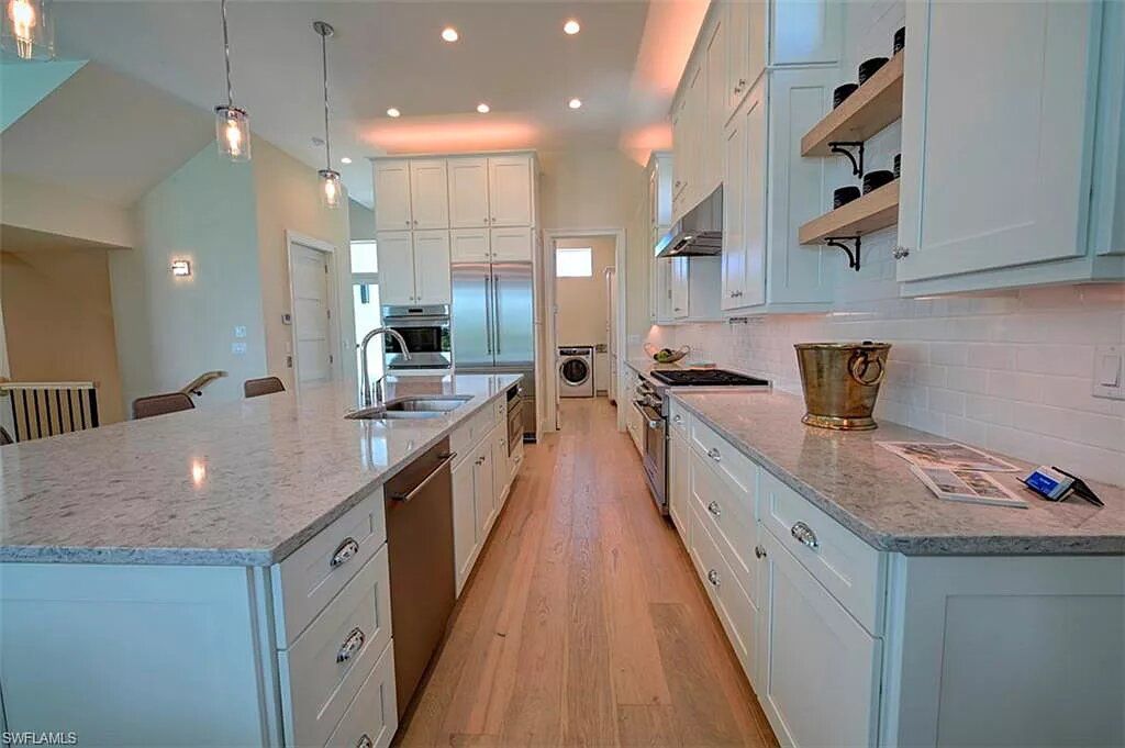Spacious white kitchen with island, stainless steel appliances, and wood flooring.