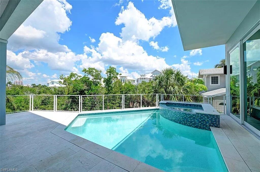 Swimming pool with blue water, white deck, and trees under a cloudy sky.