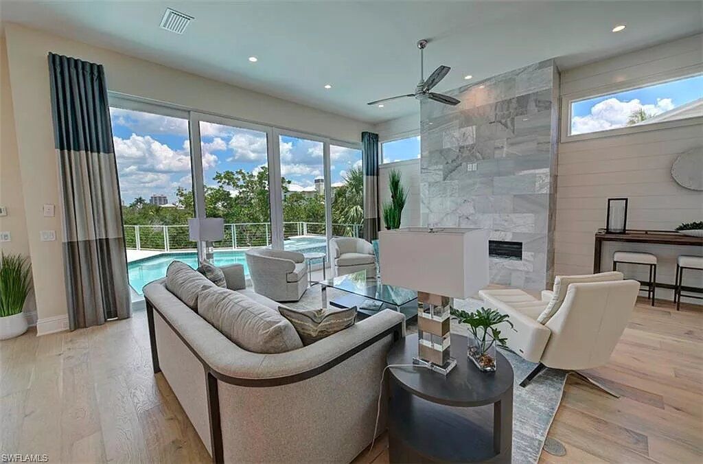 Spacious living room with pool view, light wood floors, gray sofa, fireplace, and large windows.