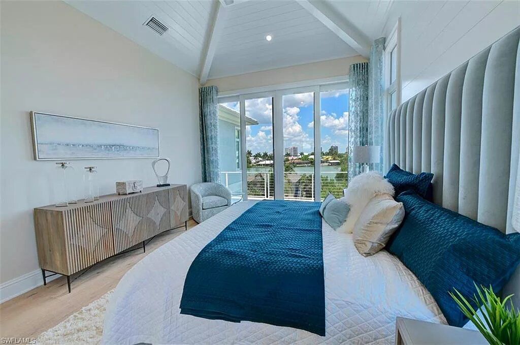 Bedroom with tall, light blue headboard, large windows, and a wooden dresser.