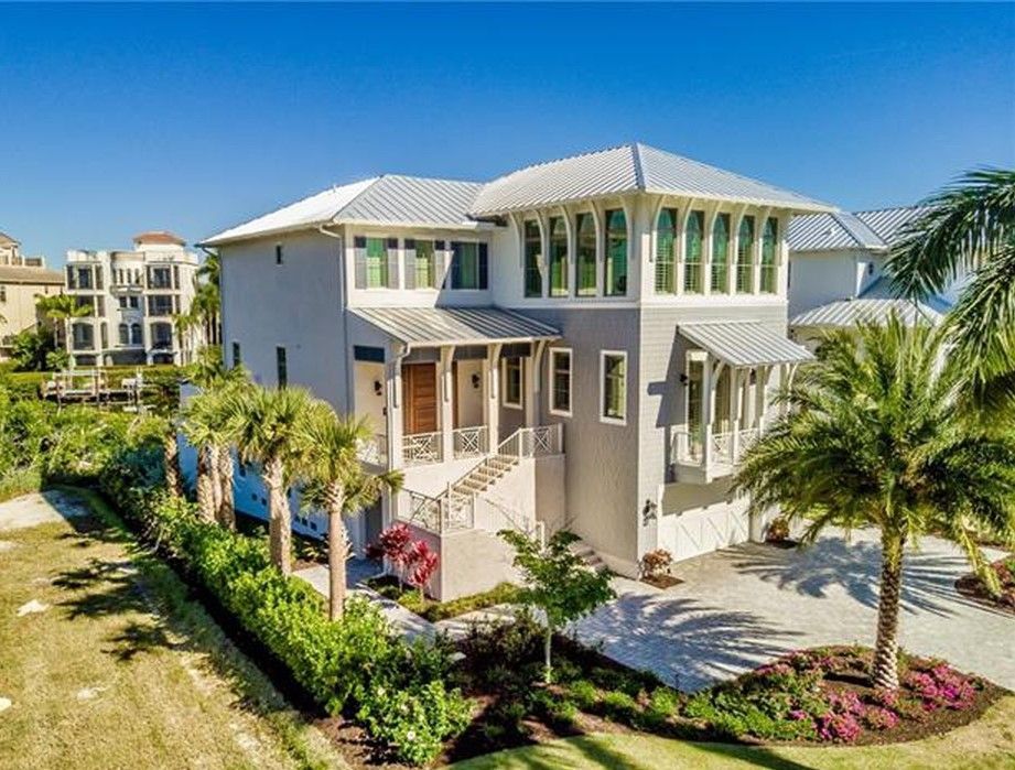 Modern two-story house with light grey exterior, white trim, and palm trees under a bright blue sky.