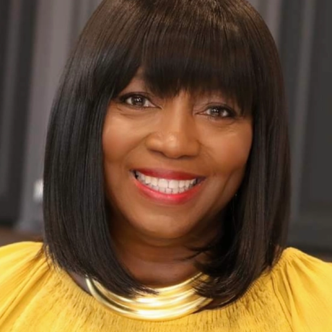 A woman wearing a yellow shirt and a gold necklace is smiling.