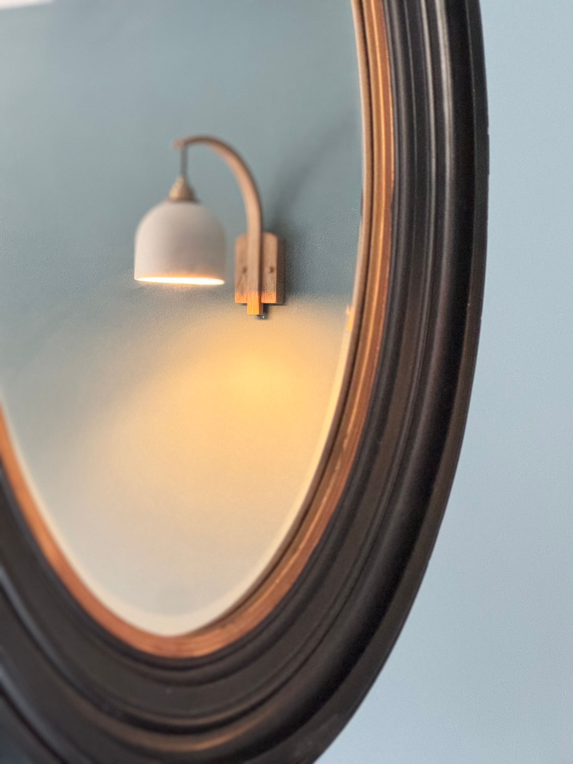 Reflection in a black-framed mirror of a wall light on a blue wall.