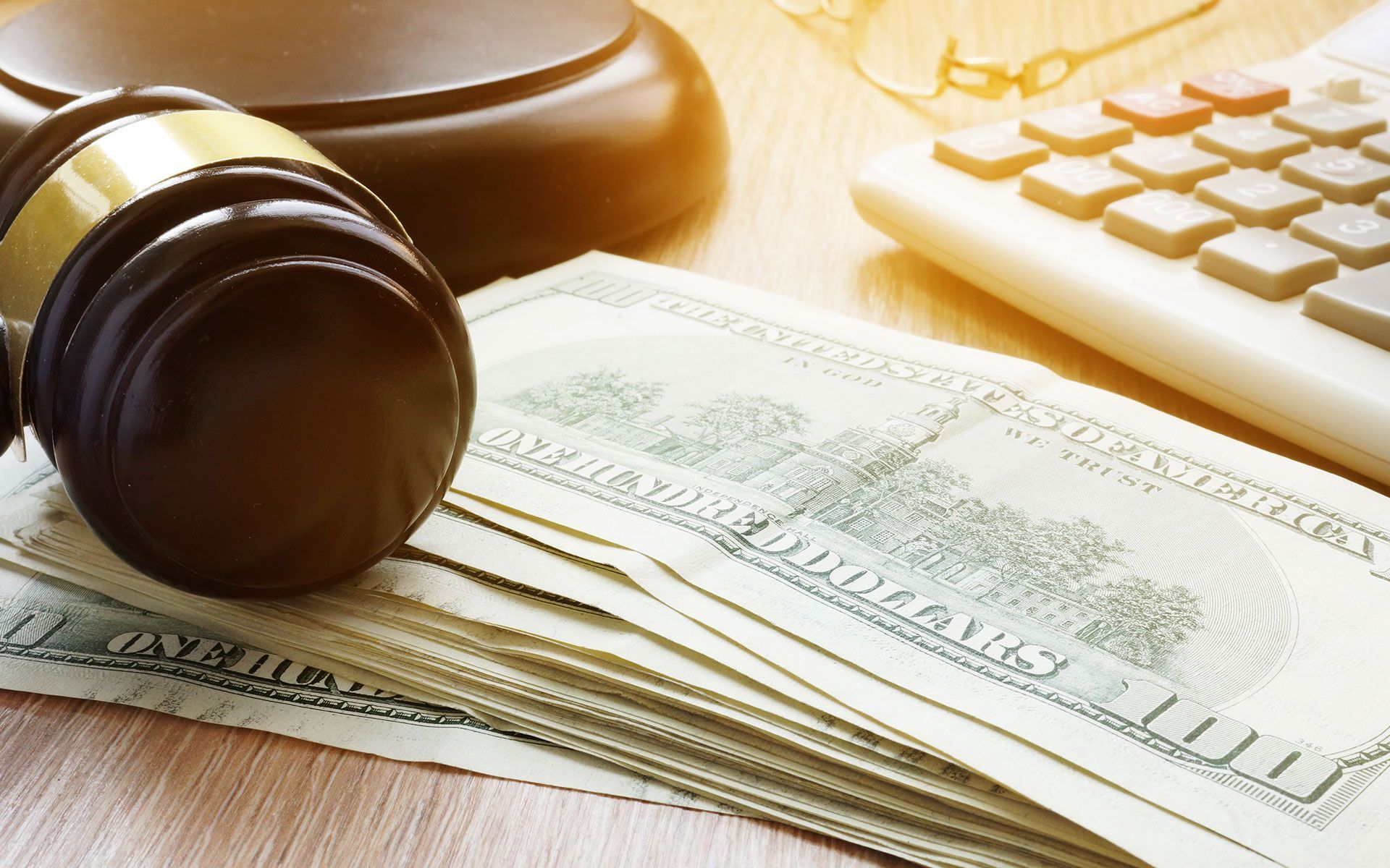 Gavel next to US dollar bills, a calculator, and glasses on a wooden surface.