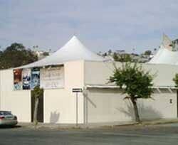 Una tienda de campaña blanca está situada encima de un edificio blanco al lado de un árbol.
