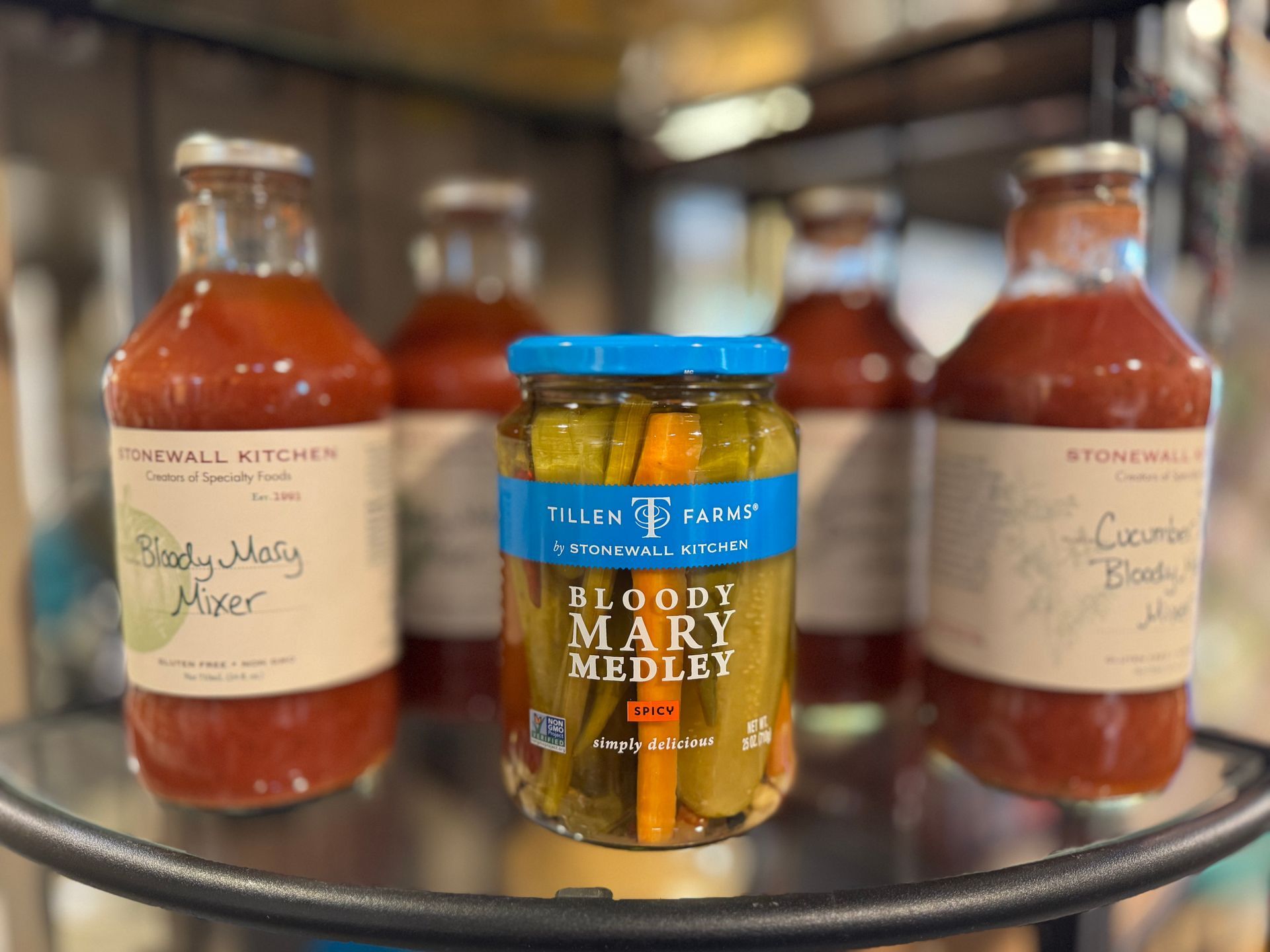 A jar of pickles is sitting on a shelf next to bottles of sauce.