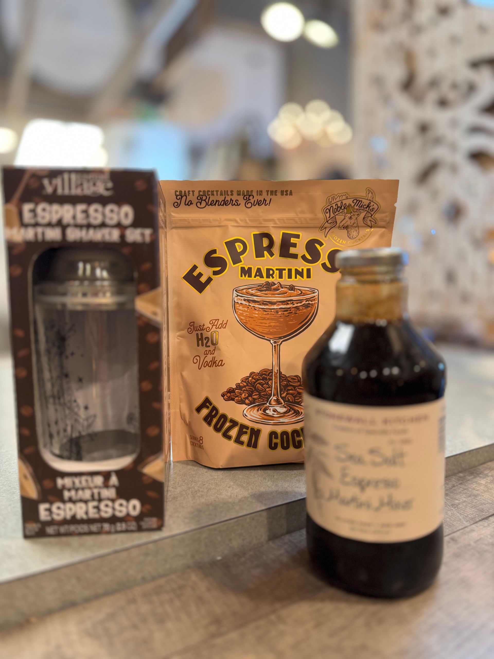 A bottle of espresso martini , a bag of espresso , and a shaker set are on a table.