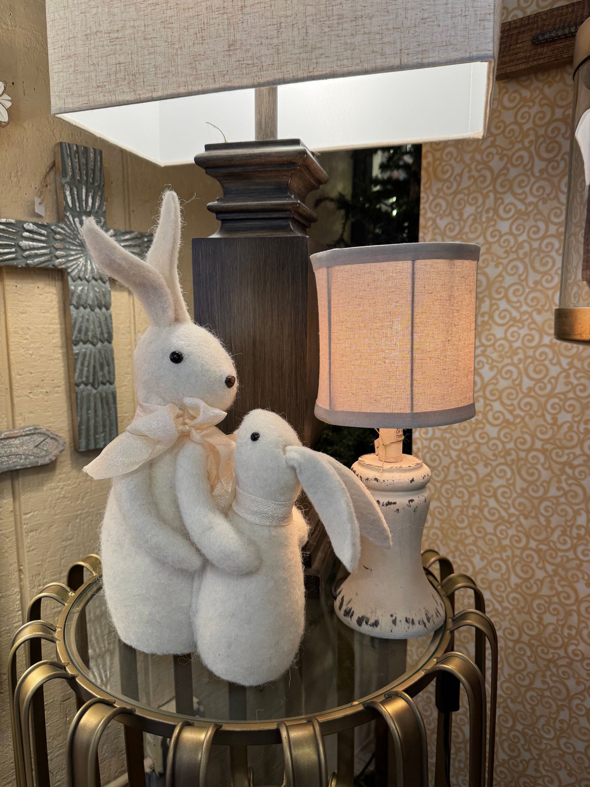 Two stuffed rabbits are sitting on a glass table next to a lamp