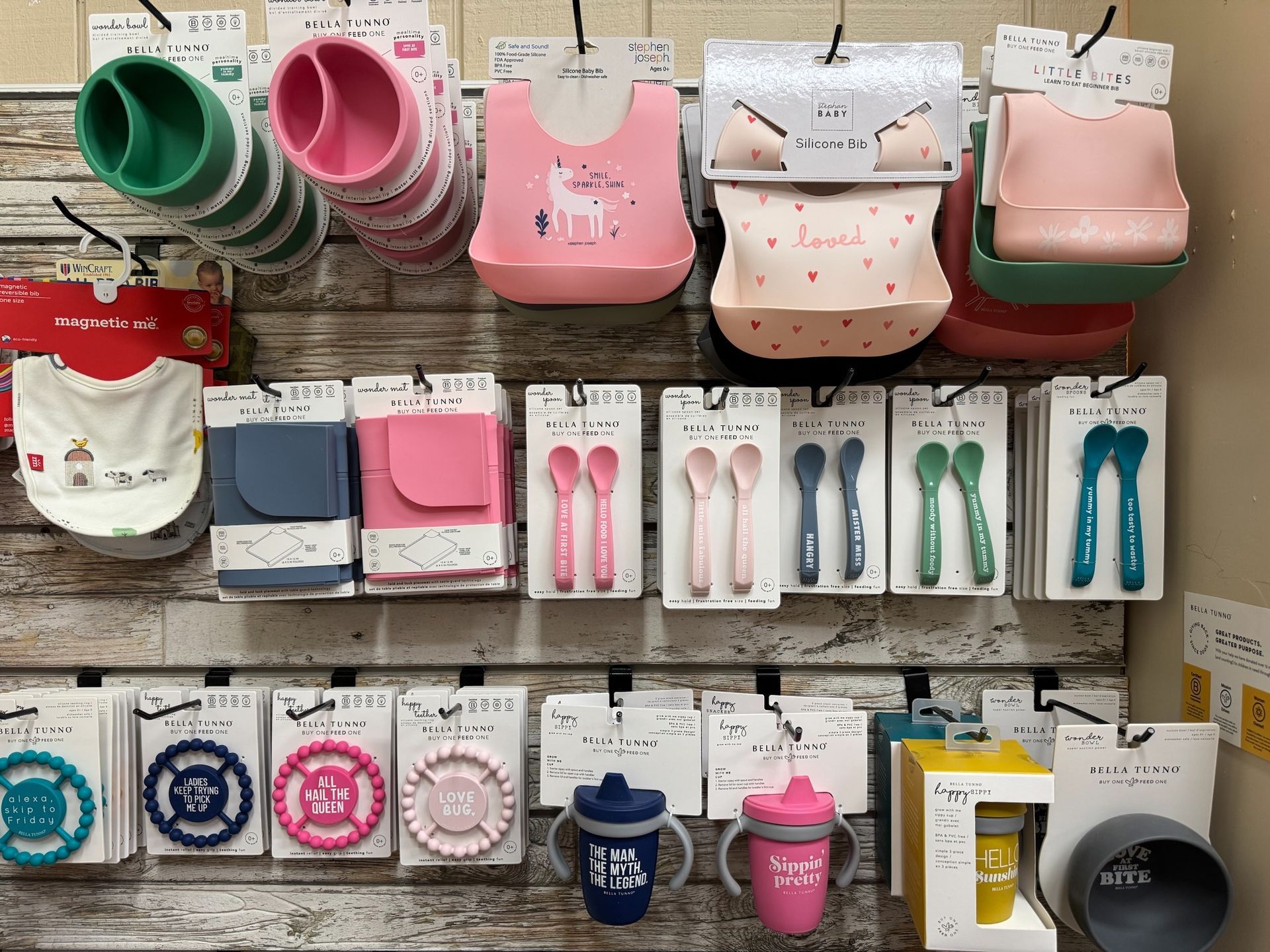 A wall filled with a variety of baby products including bibs , spoons , cups and plates.