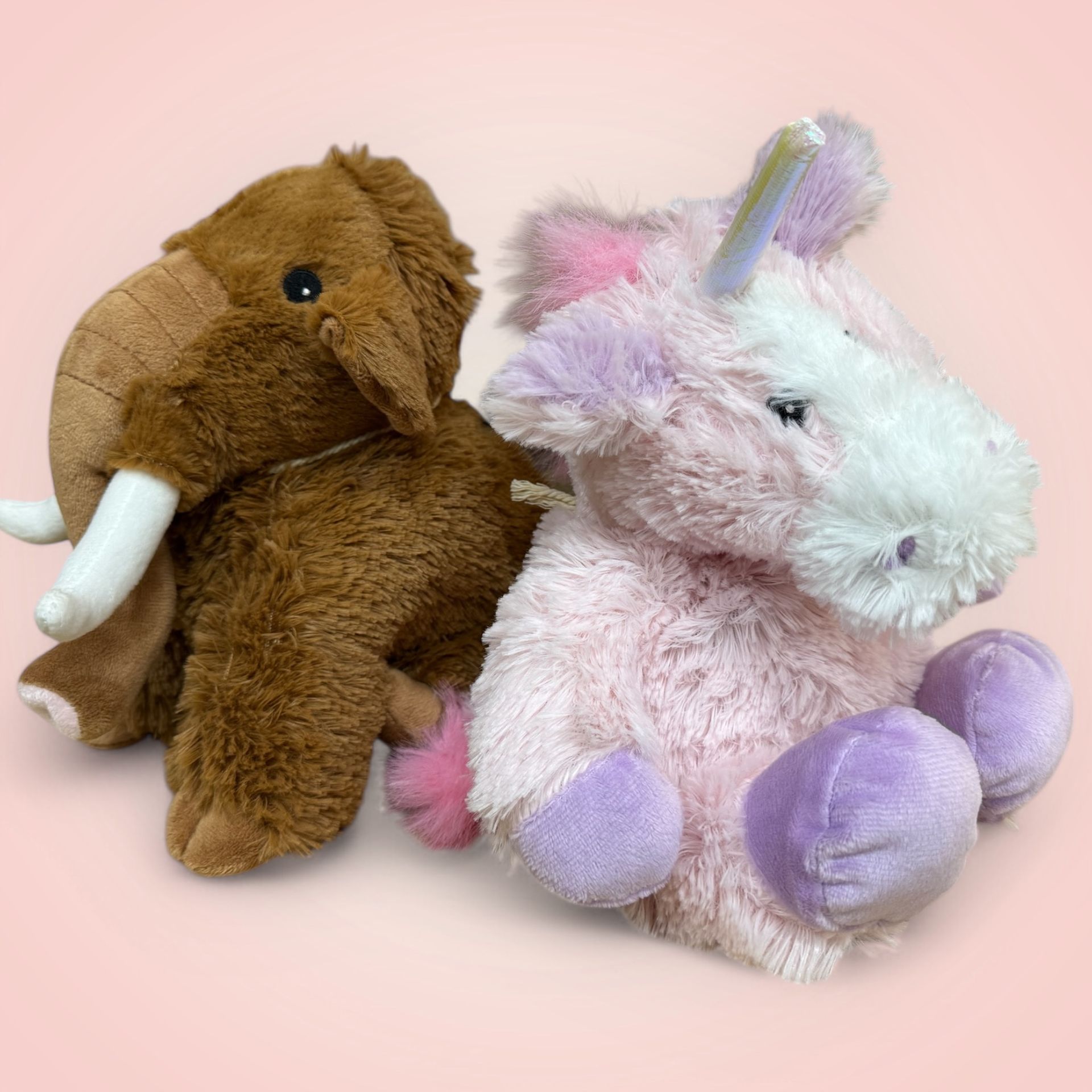 Two stuffed animals , an elephant and a unicorn , are sitting next to each other on a pink background.