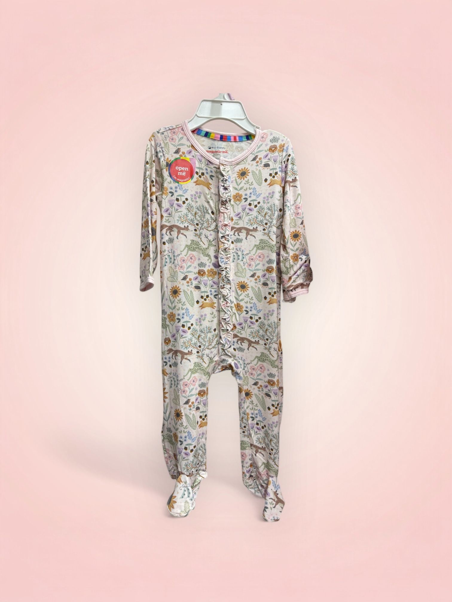 A baby onesie is hanging on a hanger on a pink background.