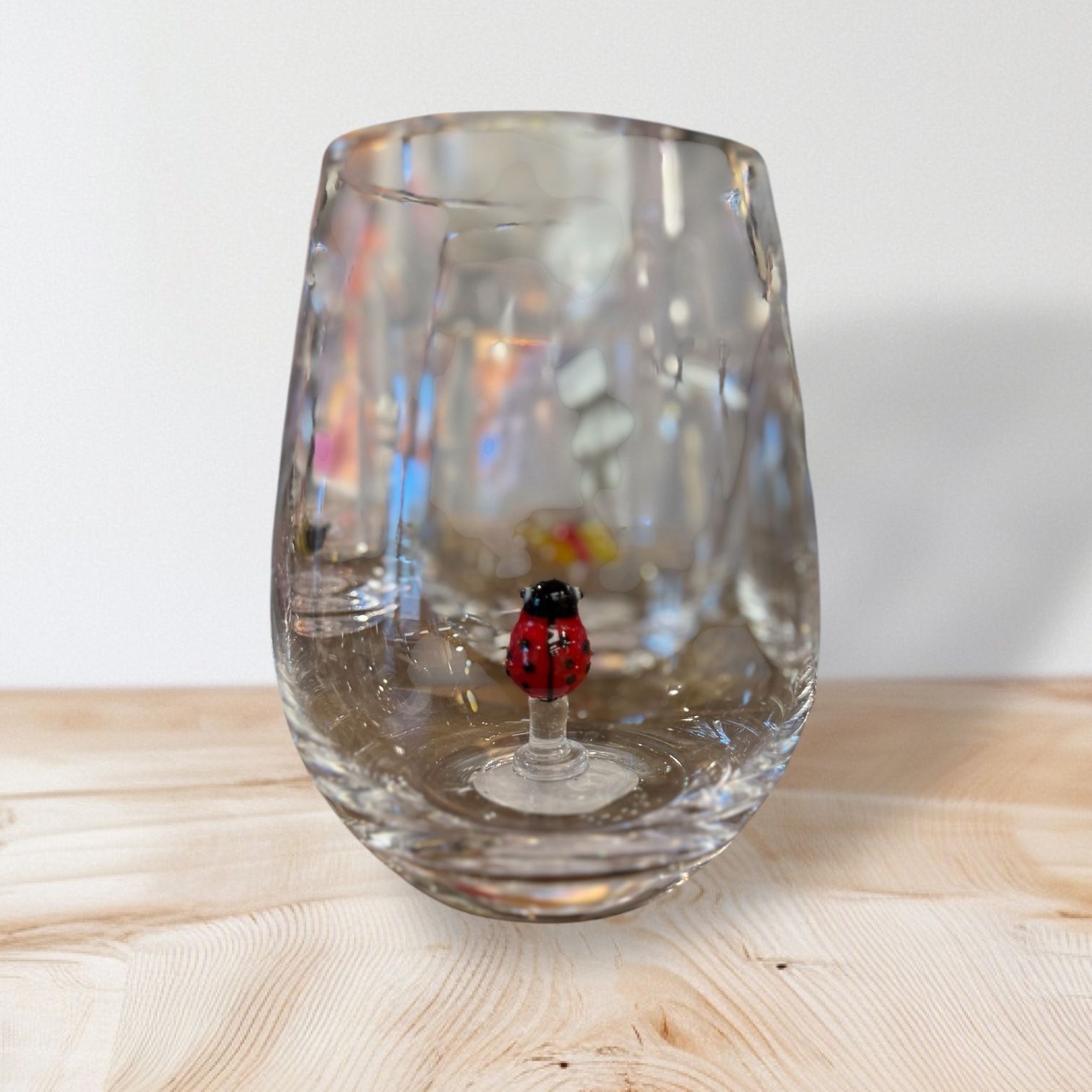 A wine glass with a ladybug on it is sitting on a wooden table.