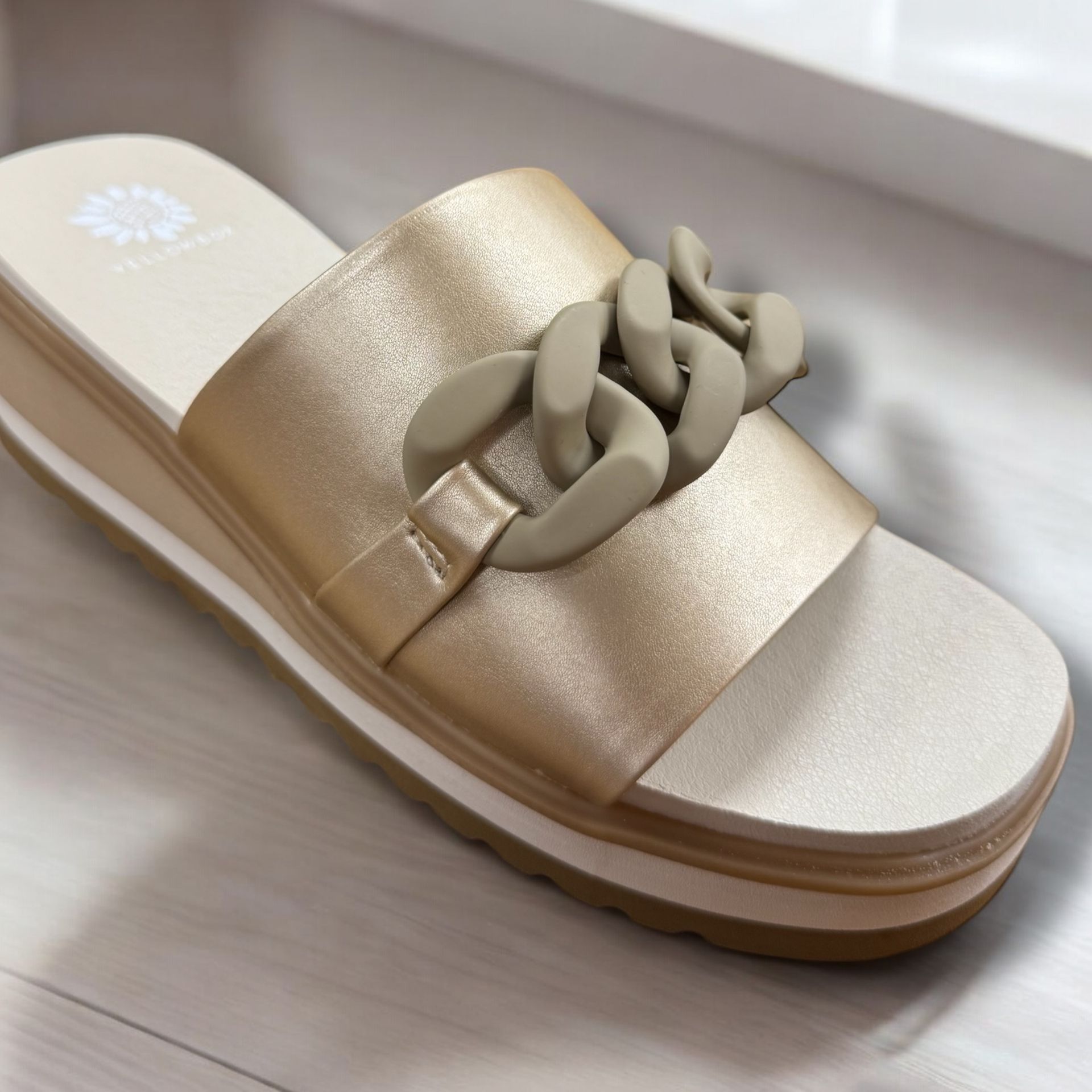 A pair of gold sandals with a chain on the side