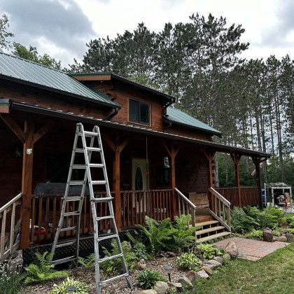 A wooden house with a green roof and a ladder on the porch.