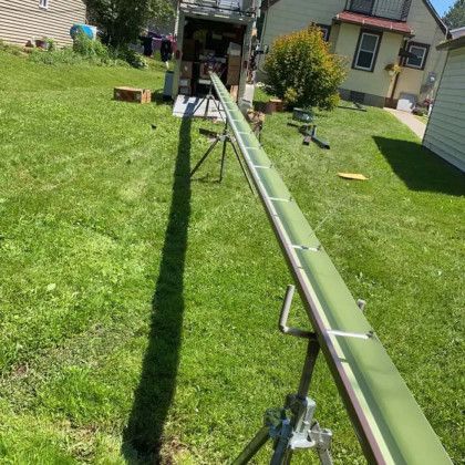 A long green pipe is sitting in the grass in front of a house.