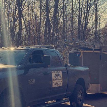 A truck is parked next to a trailer in the woods.