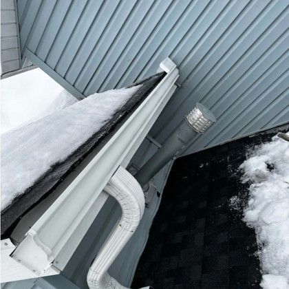 A gutter with snow on it and a light on the side of a house.