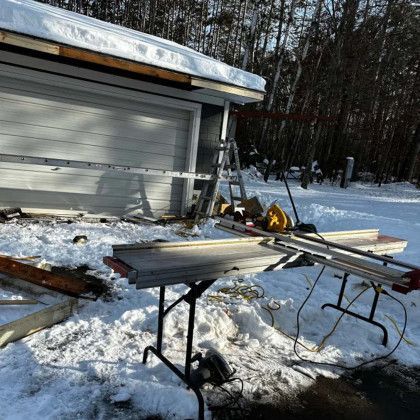 A table saw is sitting in the snow in front of a garage door.