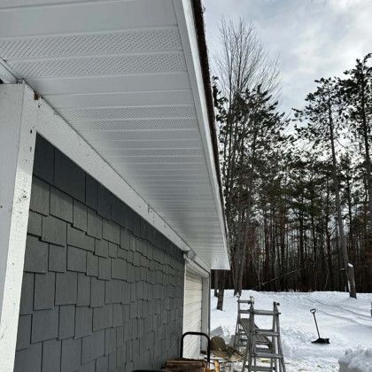 The roof of a garage with a white gutter and a ladder in the snow.
