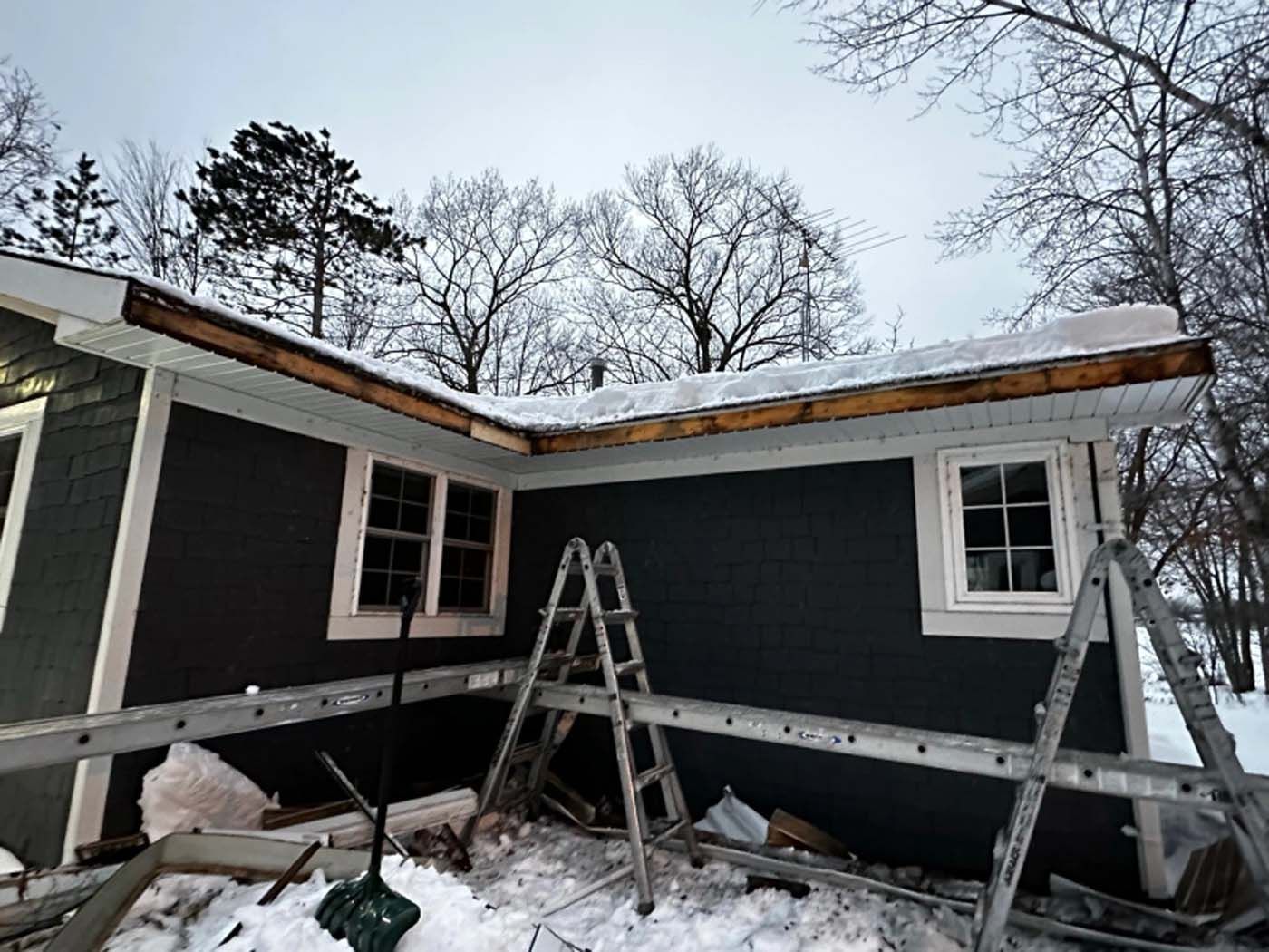 A house is being built in the snow with a ladder in front of it.