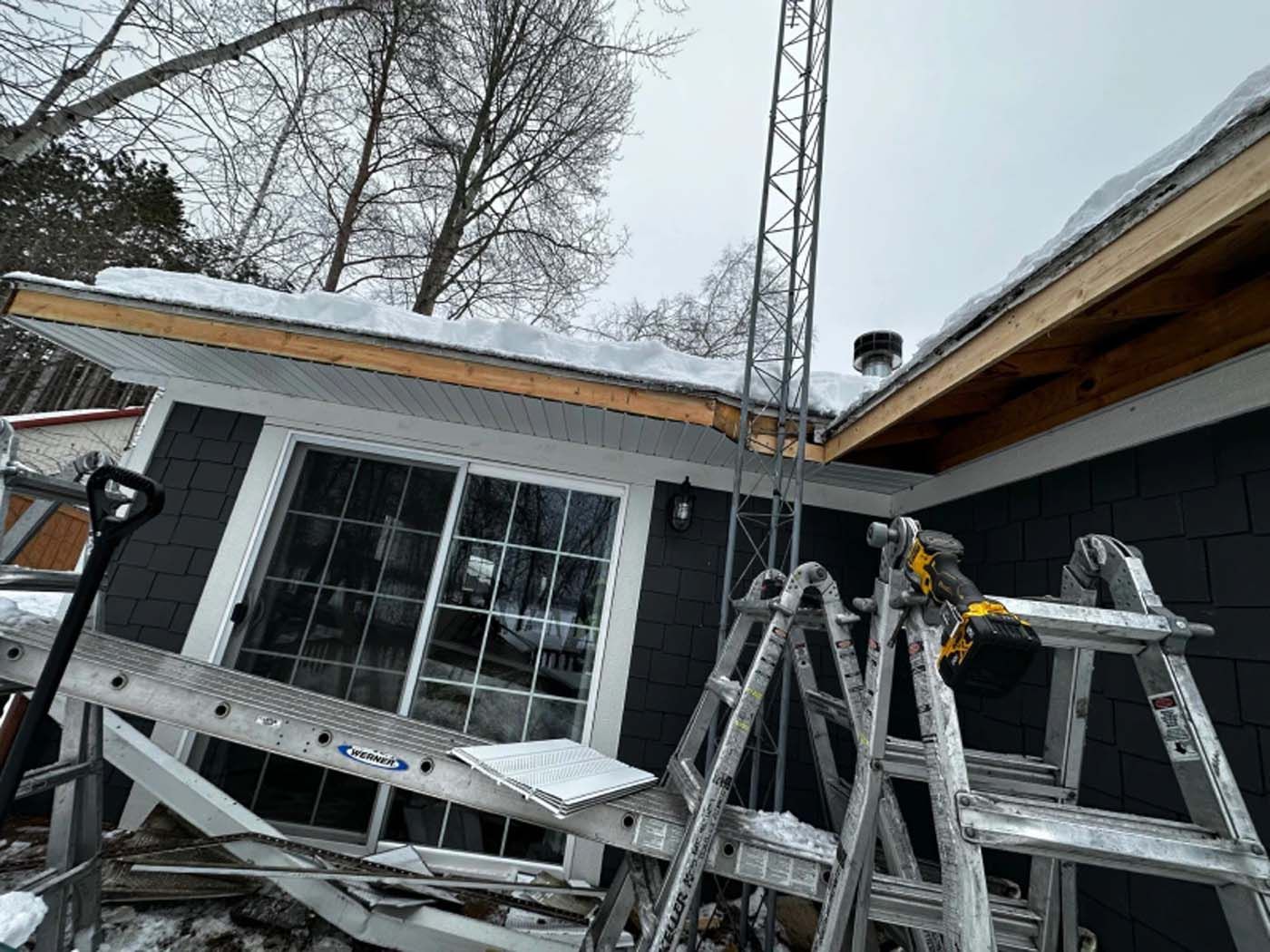 A ladder is sitting in front of a house with snow on the roof.