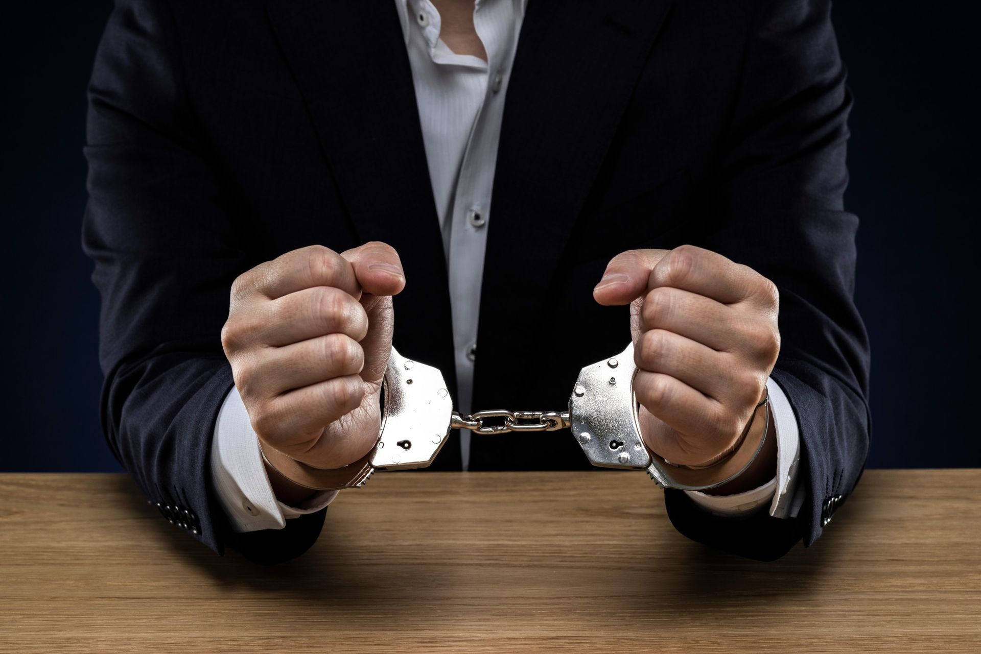 A man in a suit in need of a murder defense attorney is sitting at a table with his hands in handcuffs.