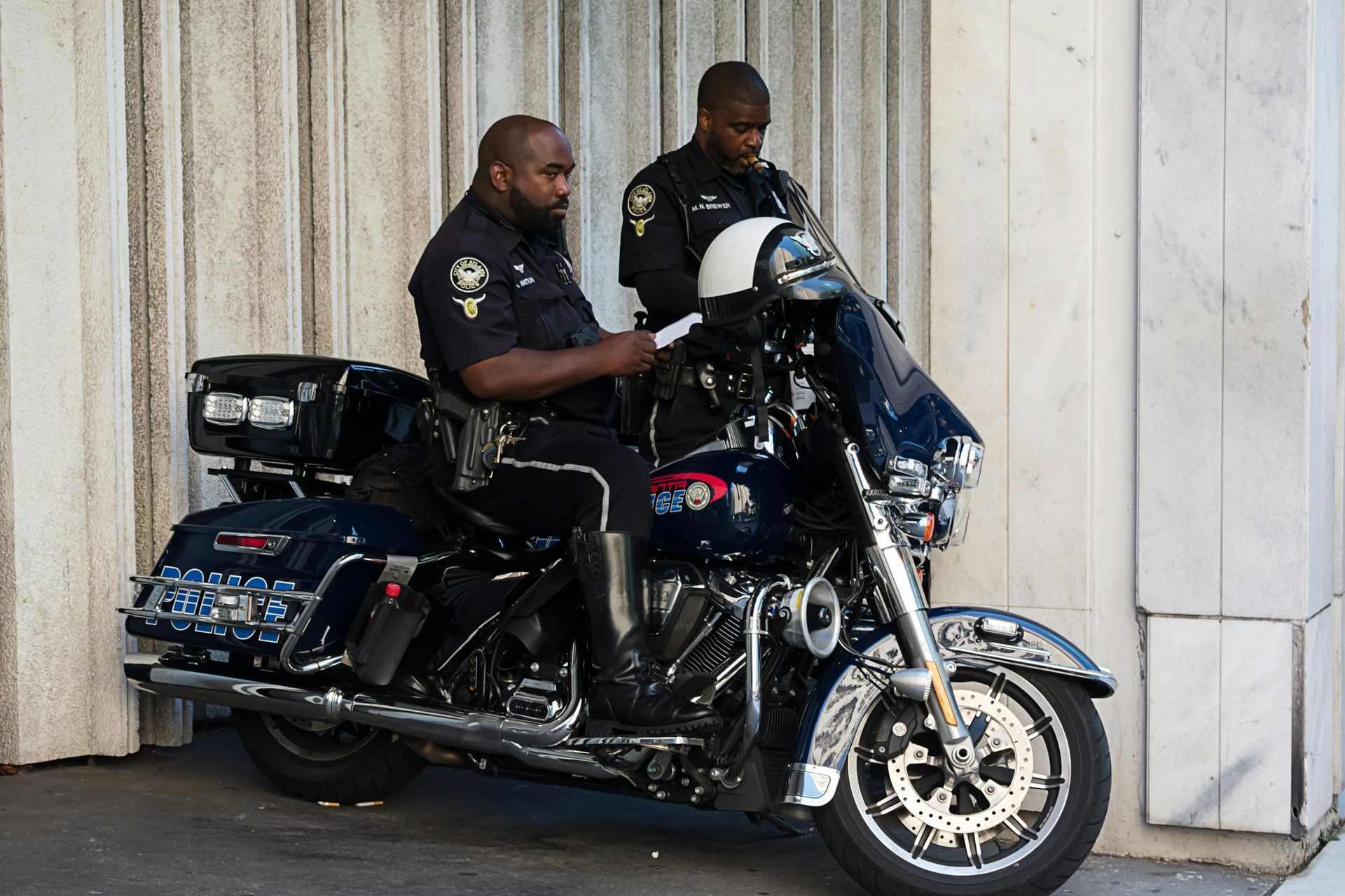 Two police officers next to a motorcycle, one writing on a clipboard, outdoors.