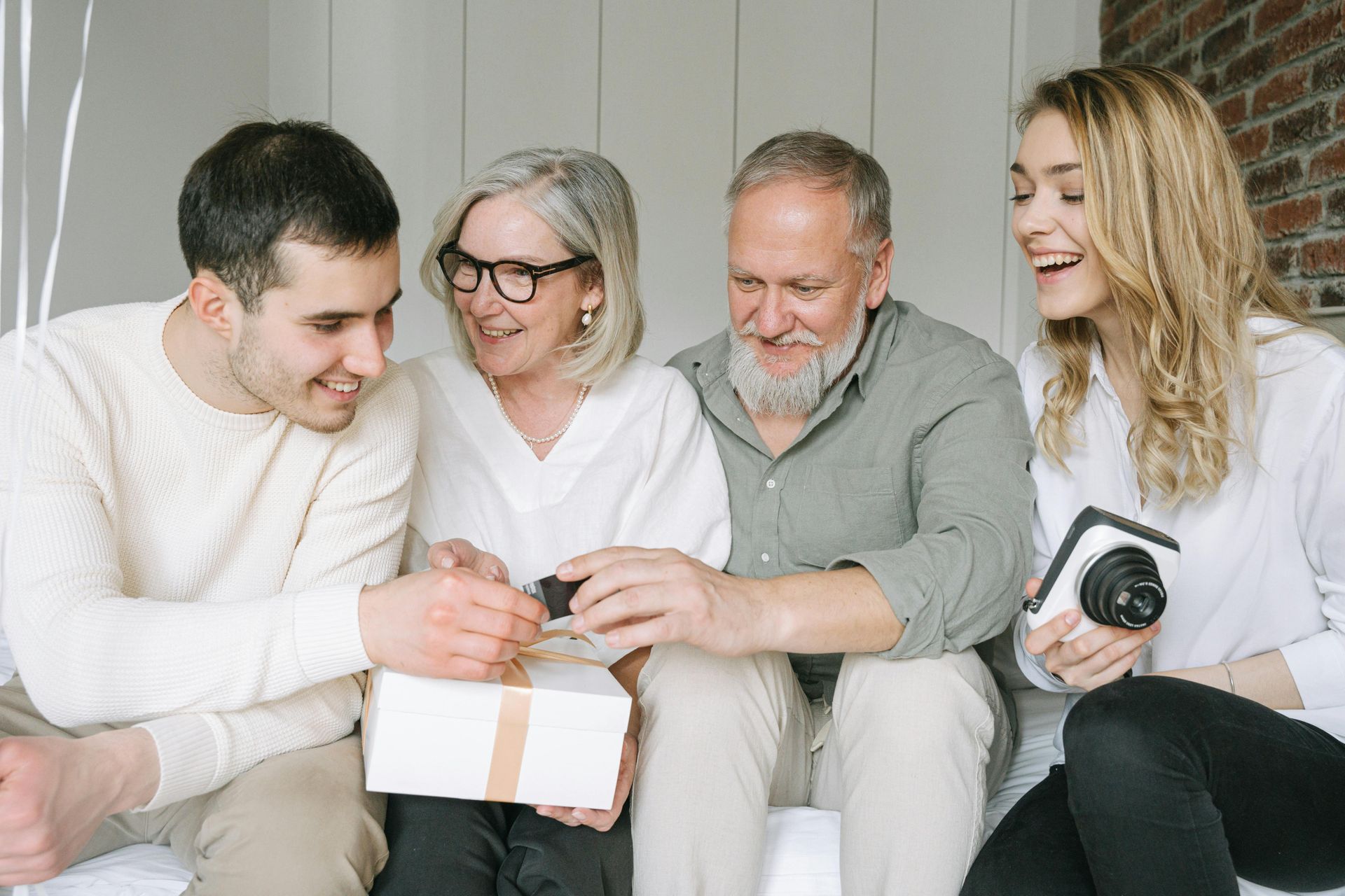 A family sits together, smiling as an older adult places a key on a wrapped gift held by a young adult.