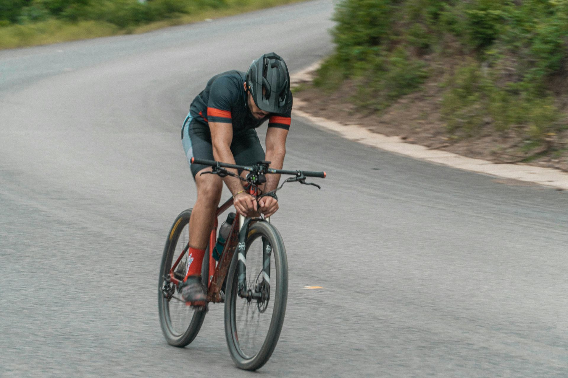 Cyclist in black helmet and gear rides a mountain bike on a paved road, leaning into a curve.
