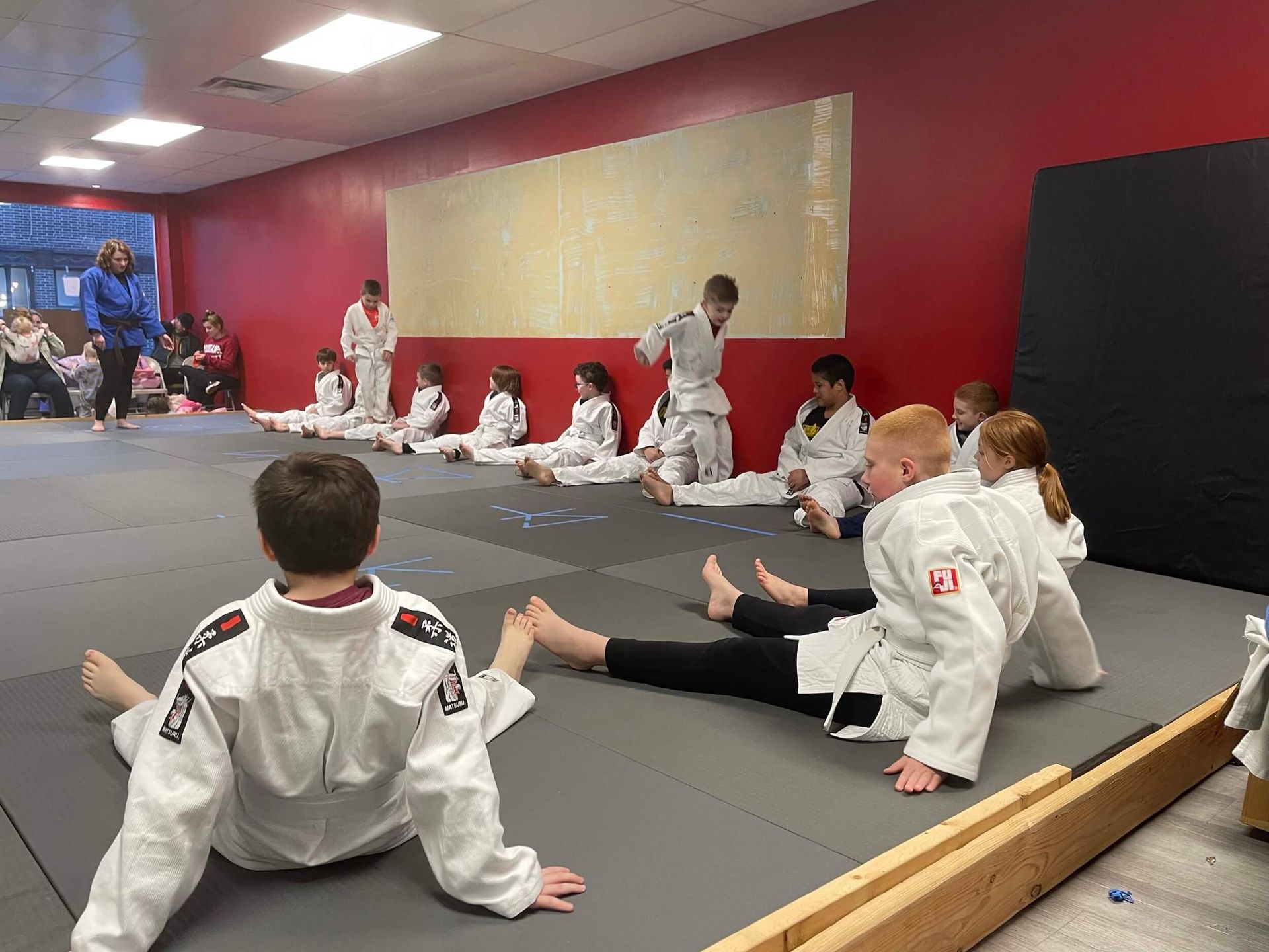 Martial arts class stretching on gray mats in a red-walled studio at Carmel Judo Indianapolis, IN